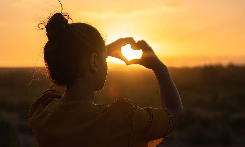 Das Bild zeigt ein Mädchen in der Sonne, welches ihre Hände zu einem Herz formt. Es steht als Metapher für die Social Media Kanäle der Praxis für Familiengesundheit. MVZ für Innere Medizin, Endokrinologie, Diabetologie und Kinder- und Jugendpsychiatrie und -psychotherapie - KJP