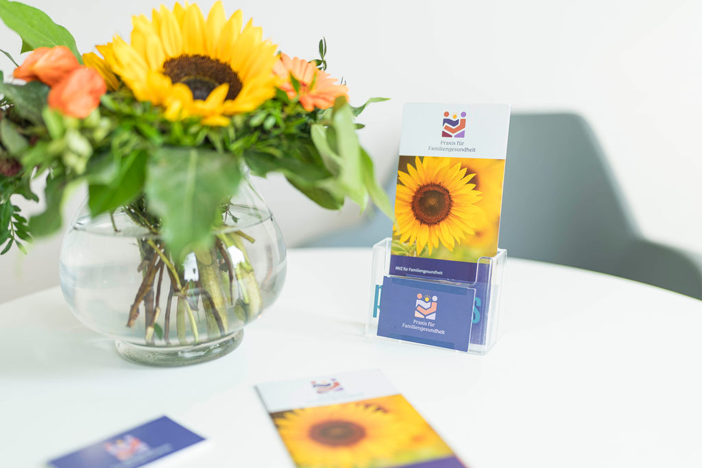 Aufnahme einer Vase mit Sonnenblumen neben einem Aufsteller mit Visitenkarten der Praxis