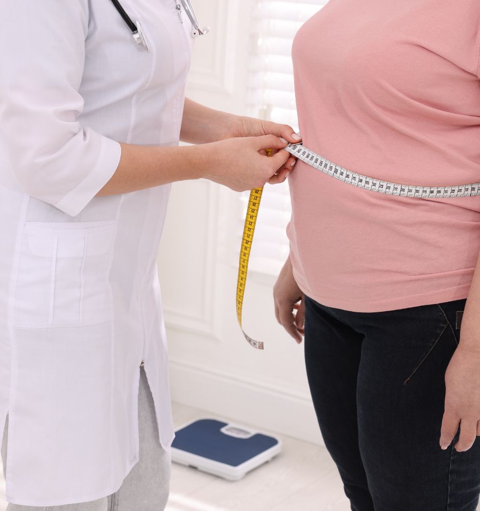 Eine übergewichtige Frau wird von einer Ärztin am Taillenumfang gemessen.